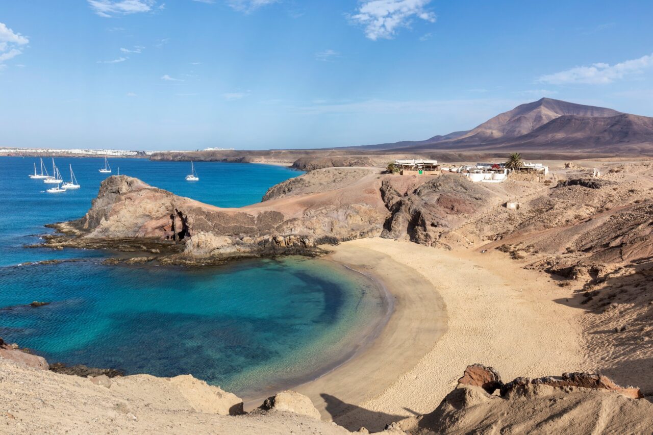 Playa de Papagayo dall’alto: la caletta a ferro di cavallo fra le scogliere, con le barche e Playa Blanca sullo sfondo